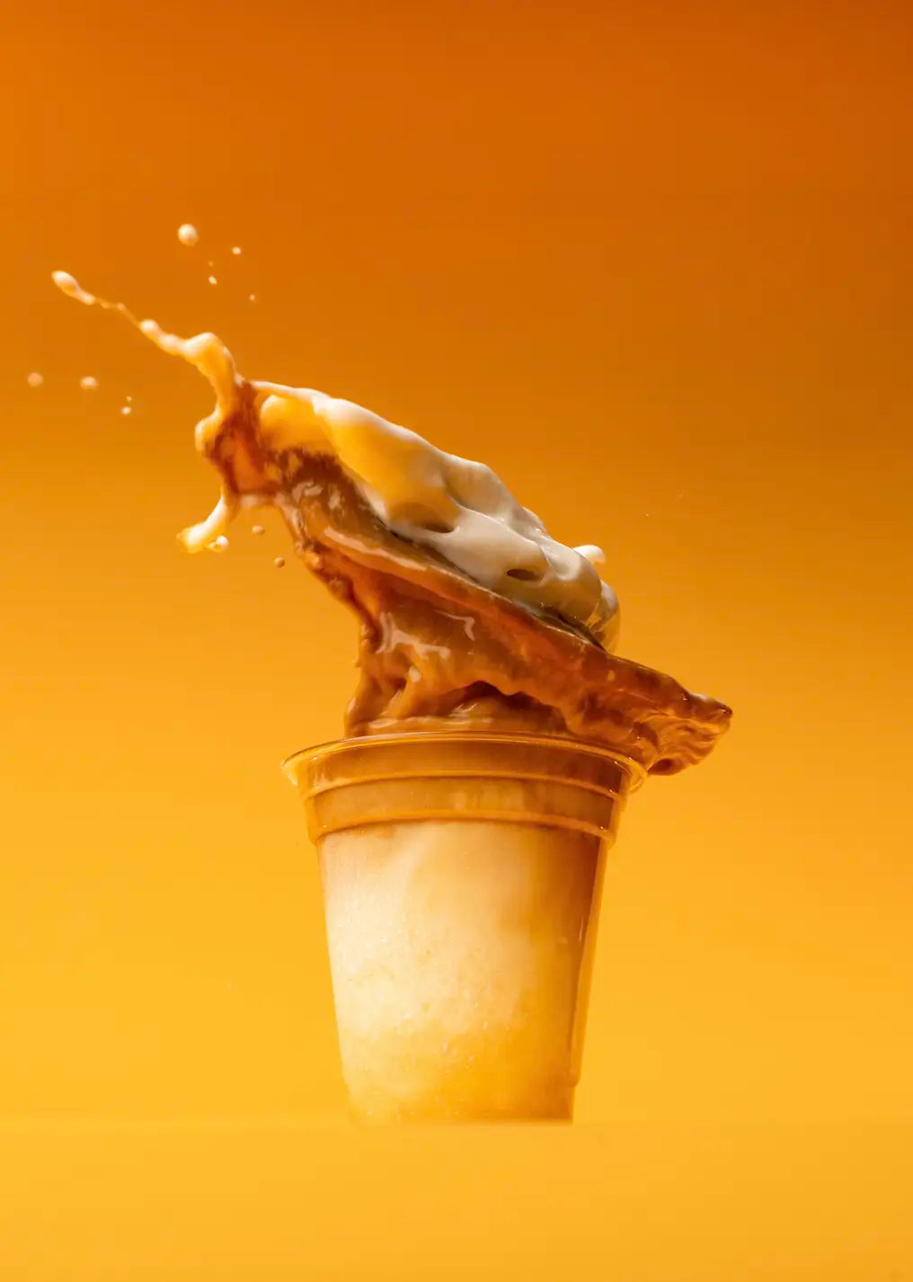 Iced coffee splashing out of the cup on an orange background