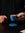 Tattooed man in black t-shirt holding blue espresso cup above blue coaster on a black table